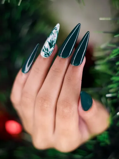 For a more elegant holiday style, I created this set using a deep forest green polish on stiletto nails. The look is elevated with a single white accent nail featuring delicate, hand-painted foliage art.