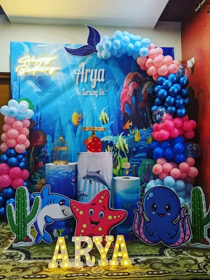 An immersive underwater theme birthday party for a sixth birthday celebration. This detailed setup includes a vibrant ocean backdrop, character cutouts of a shark and octopus, marquee letters, and themed balloon columns.