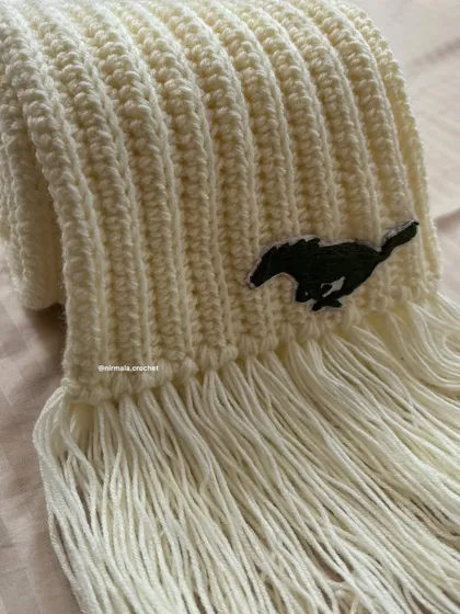 A close-up of the custom embroidered Mustang logo on our cream ribbed muffler. We take care to get the details just right for every personalized order.