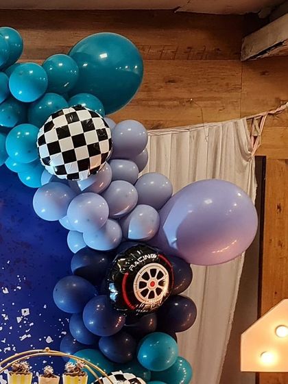 A close-up of a race car-themed balloon garland. The mix of blues is accented with a checkered flag balloon and a racing tire foil balloon, adding authentic details to the theme.