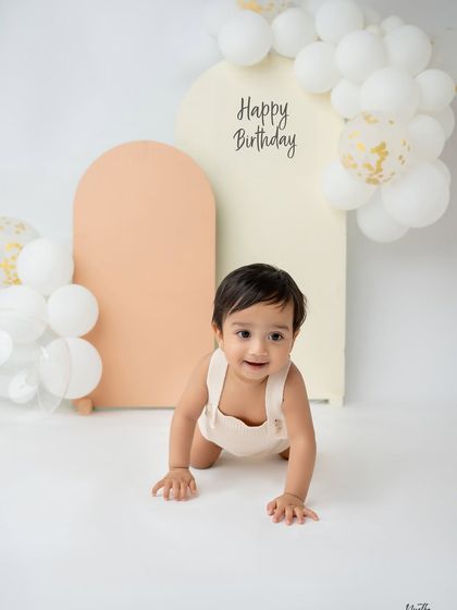 A simple and modern first birthday setup with pastel-colored arches and white balloons. This little one is on the move!