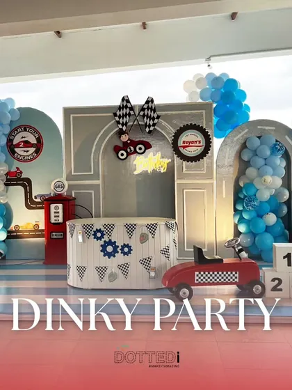 For a little one who loves cars, I created this 'Dinky Party' theme. The setup features a custom backdrop with a gas station, traffic lights, and checkered flag details, all framed by blue and white balloon garlands to get the engines started.