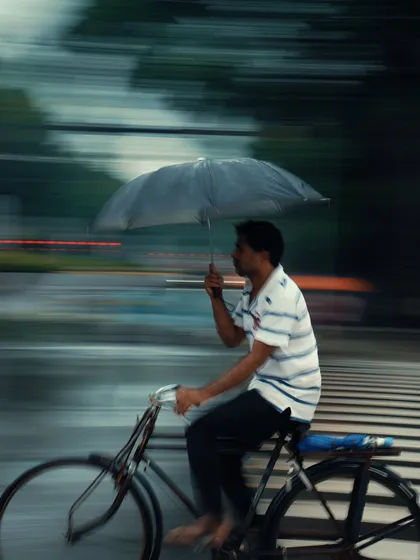 A man on a bicycle holds an umbrella while riding, captured with a panning motion blur. This technique conveys a sense of speed and urgency, a signature of my street photography style.