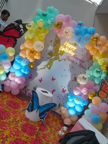 A rainbow butterfly and fairy theme for a 5th birthday. This setup includes a personalized backdrop, a multi-colored balloon arch, and large butterfly cutouts.