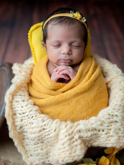 A sweet close-up of the baby with hands clasped, looking serene in the sunflower-themed basket.