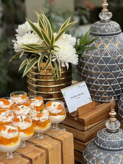 An elegant dessert display featuring our mango cream verrines, set against beautiful decorative urns.