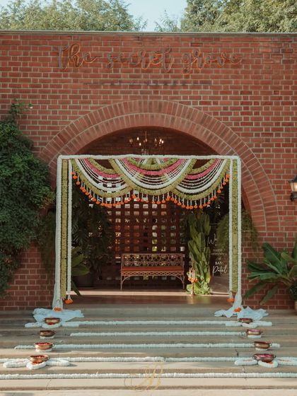 The entrance arch for a naming ceremony, beautifully crafted with woven coconut leaf garlands, white chrysanthemums, and bright orange marigolds, set against the venue's brick architecture.