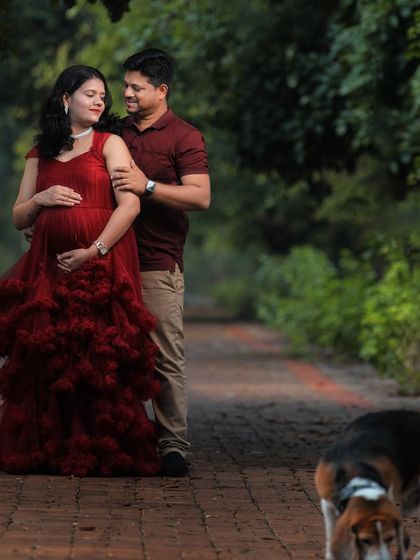 A sweet couple's moment during their maternity shoot, with their furry friend making a surprise appearance. The red ruffled gown adds a pop of color to the park setting.