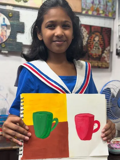 Look at that proud smile. One of our youngest artists shows off her work from a foundational drawing class where she learned about color, shape, and composition by painting simple objects like mugs.