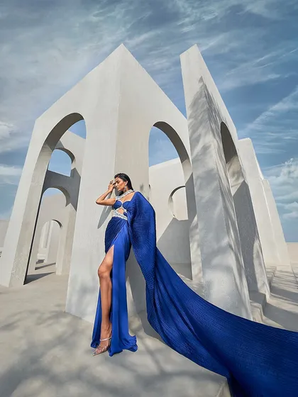 This pre-draped sari gown in a vivid blue is designed for dramatic impact. The crushed fabric creates a liquid-like flow, culminating in a floor-sweeping trail that moves with breathtaking elegance.