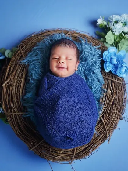 Capturing that perfect, sleepy newborn smile is my specialty. For this shot, I used a cozy nest prop with a vibrant blue theme, complete with floral accents, to create a peaceful and visually striking portrait.