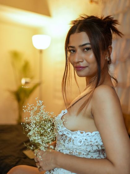 A soft and romantic indoor portrait, using warm lamp light to create a cozy atmosphere. The delicate flowers add a gentle, feminine touch.