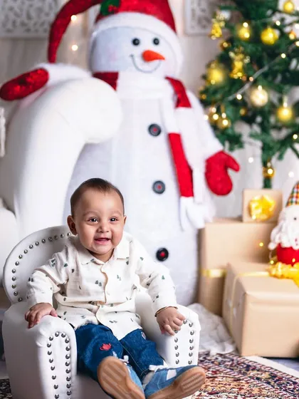 A joyful little boy in his own mini armchair, surrounded by presents and the twinkling lights of the Christmas tree.