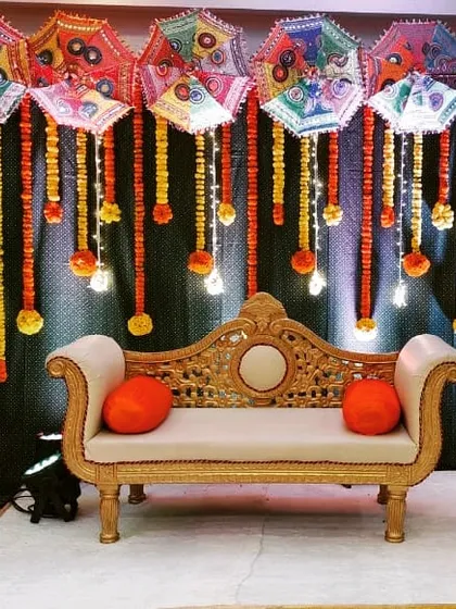 For a vibrant Haldi or Mehendi ceremony, I offer colorful backdrops like this one. This setup features a rental package with a traditional sofa, marigold garlands, and a canopy of decorative Rajasthani umbrellas.