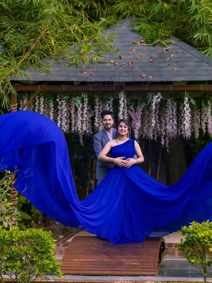 A dramatic shot of a flowing blue gown on a wooden bridge, with the garden's bamboo and wisteria-covered gazebo in the background.