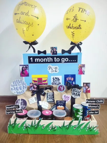 The wedding countdown is an exciting time, and this "1 month to go" hamper is designed to celebrate it. I've included a variety of food items like noodles, momos, and cake jars, along with personal photos and fun stickers, all arranged in a decorative tray to build anticipation for the wedding day.