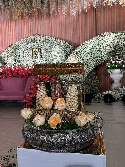 A decorative dry fruit holder, elegantly arranged with roses, as part of an offering display.