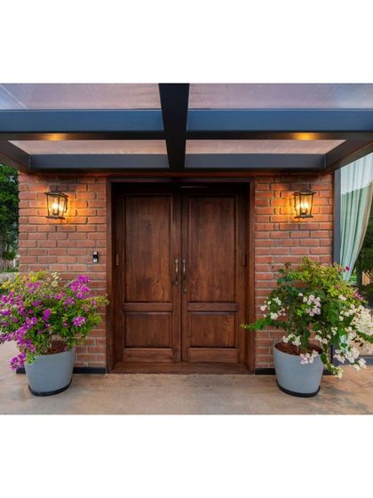The main entrance of the Nandi Hills home, featuring a solid wood double door set against an exposed brick wall. Potted bougainvillea adds a splash of color, creating a warm and rustic welcome that hints at the natural aesthetic within.