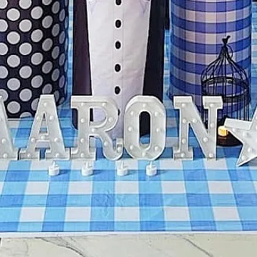 Light-up marquee letters spelling out the name 'AARON' against a blue gingham floor mat, part of a detailed Boss Baby party.
