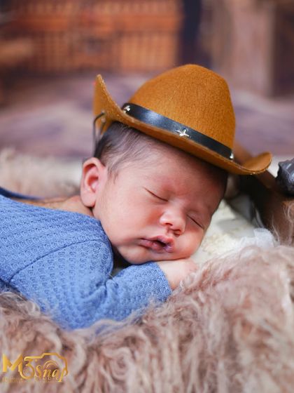 A close-up of a newborn wearing a cowboy hat, sleeping on a soft fur blanket. The texture and warm tones make this shot incredibly cozy.