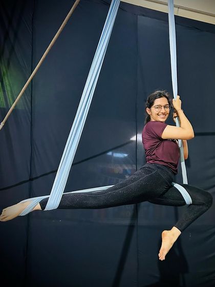 A smiling student demonstrates a suspended split, showing the joy and confidence that comes from mastering new aerial yoga poses.