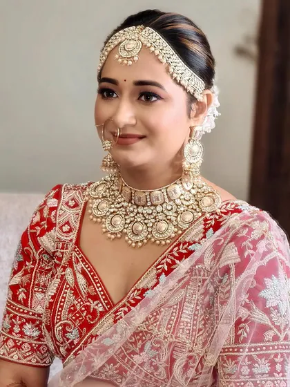 A close-up portrait showcasing the beautiful details of her matha patti and the soft, blended makeup that complements her traditional red and white lehenga.