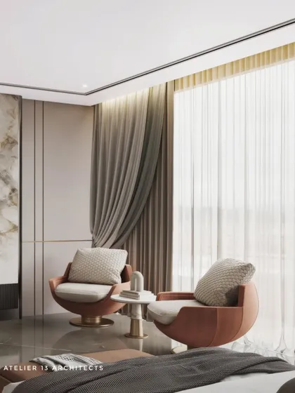 A cozy seating nook within a modern bedroom, featuring two comfortable tan swivel chairs. The room's design includes a marble media unit with an integrated electric fireplace below, adding warmth and ambiance.