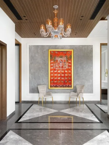 The entrance foyer, where a bold geometric pattern in the marble floor leads the eye towards a stunning Pichwai painting. The amber crystal chandelier and wood-paneled ceiling add layers of warmth and luxury.