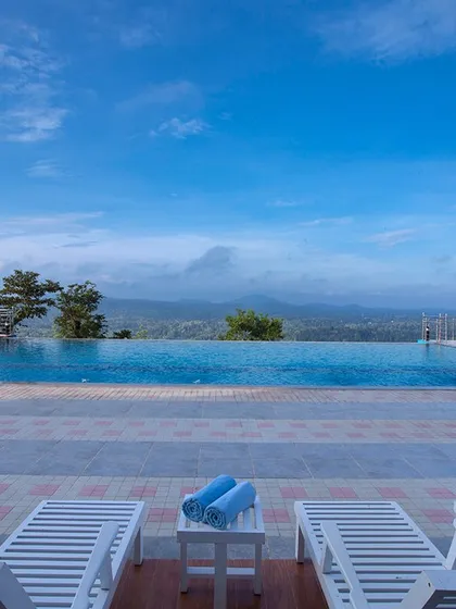 Another view of the infinity pool at Coorg Cliffs Resort, with comfortable lounge chairs ready for a day of relaxation with spectacular mountain and forest views.
