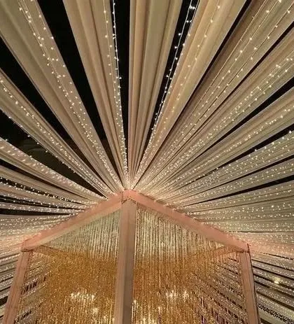 A beautiful ceiling treatment with drapes and fairy lights radiating from the center. This design adds a touch of glamour and grandeur to any indoor or tented venue.