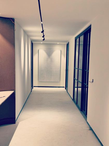 This corridor was designed to create a sense of calm as it leads to the private spaces of the home. Clean white walls, a seamless floor, and minimalist track lighting create a serene pathway. A large piece of textured white art at the end of the hall serves as a subtle focal point.