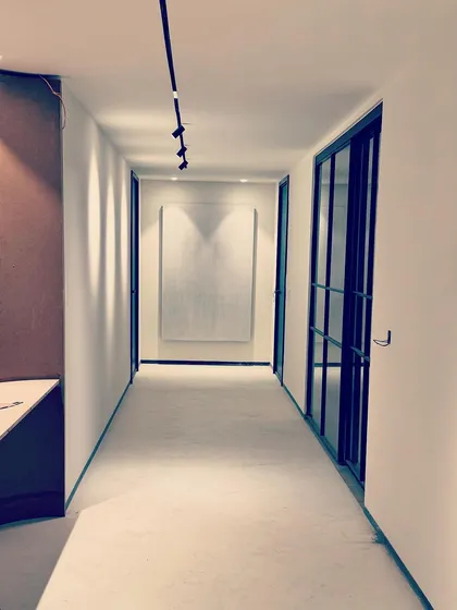 This corridor was designed to create a sense of calm as it leads to the private spaces of the home. Clean white walls, a seamless floor, and minimalist track lighting create a serene pathway. A large piece of textured white art at the end of the hall serves as a subtle focal point.
