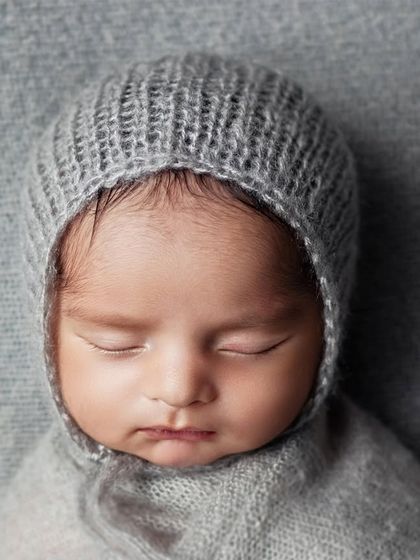A close-up on this peacefully sleeping baby, wearing a soft grey knitted bonnet. The focus is entirely on their perfect, tiny features.