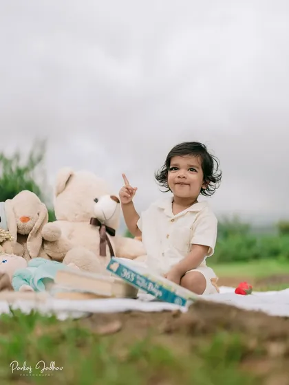 One year old and already pointing to the sky! This adorable solo portrait of the birthday boy captures his curious spirit amidst his favorite toys during his outdoor celebration.