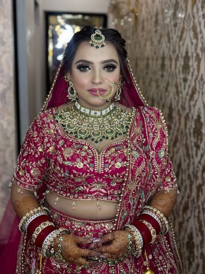 This bride is glowing in her traditional pink lehenga and green jewelry. The makeup is perfectly balanced to enhance her features without overpowering her natural beauty.
