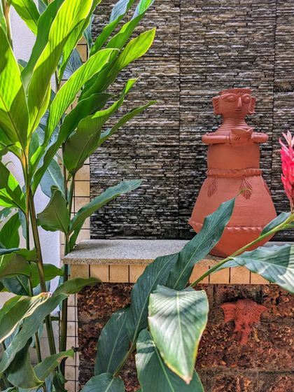 A traditional terracotta statue is nestled among lush green foliage against a stacked stone wall. I enjoy incorporating art and personal objects into the garden to create unique focal points.