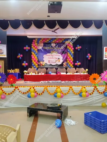 A professional stage decoration for a school or college graduation day celebration. This setup includes a large balloon arch over the main banner, balloon pillars, and floral arrangements along the stage front, suitable for any formal function.