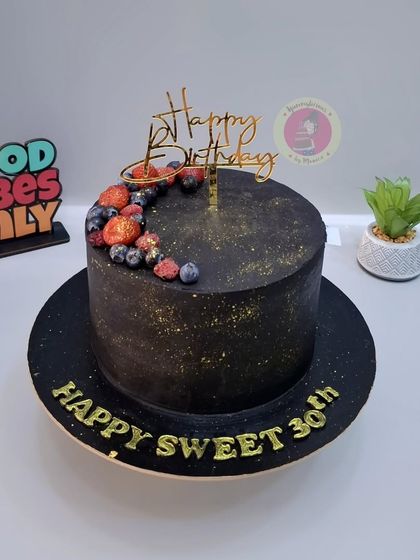 A sophisticated black ganache cake for a 30th birthday, decorated with fresh berries and a touch of gold dust.