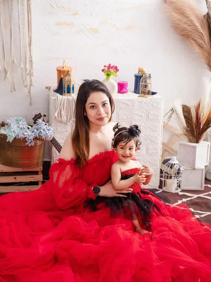 A mother in a stunning red gown holds her little girl, a beautiful and dramatic portrait of motherly love.