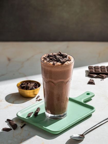 A rich dark chocolate milkshake, topped with chocolate shavings and styled with pieces of a chocolate bar.
