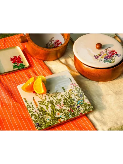 An outdoor 'golden hour' shot of a tablescape with wooden bowls and floral-painted plates. The warm, natural light gives the products a beautiful glow.