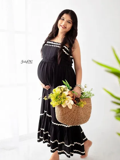 A bright and airy solo portrait. The simple black dress and a basket of flowers against the white background create a fresh, happy, and casual maternity photo.