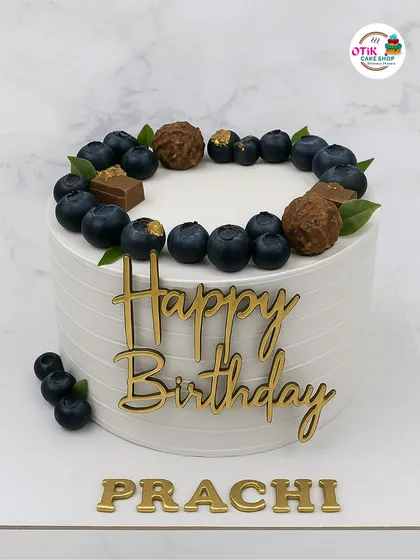 This cake shows our love for elegant and minimalist designs. A clean, white buttercream finish is topped with fresh blueberries, chocolate truffles, and a personalized gold acrylic nameplate for a sophisticated birthday celebration.