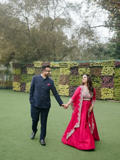 A happy couple walks hand-in-hand across a lush green lawn during their Roka ceremony, sharing a look of love.