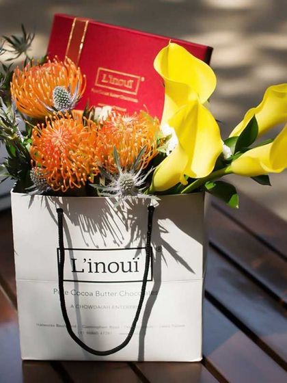 A beautifully curated gift bag featuring a box of our chocolates nestled amongst exotic flowers. We specialize in creating bespoke gifts that feel personal and luxurious.