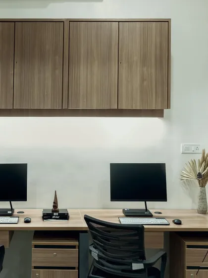A close-up of the workstations, showing the simple yet effective combination of wood-laminate desks and dark, floating overhead cabinets for storage. The under-cabinet lighting provides excellent task lighting.