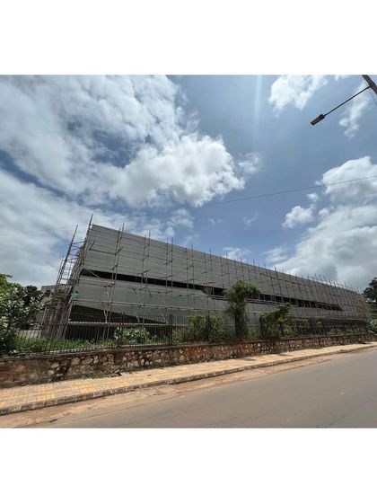 The sports center under construction, with scaffolding covering the facade. This view from the road shows the building's significant scale and linear form.