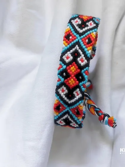 A close-up of a complex geometric pattern bracelet. The combination of black, white, red, and turquoise creates a striking design.