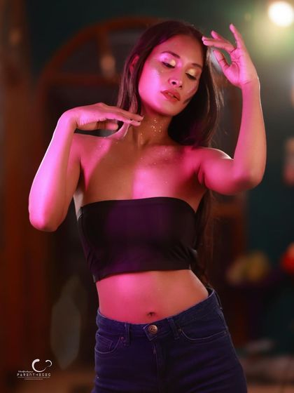 A graceful and expressive pose. The pink and green lighting adds a dreamy, otherworldly feel to this glitter-adorned portrait.