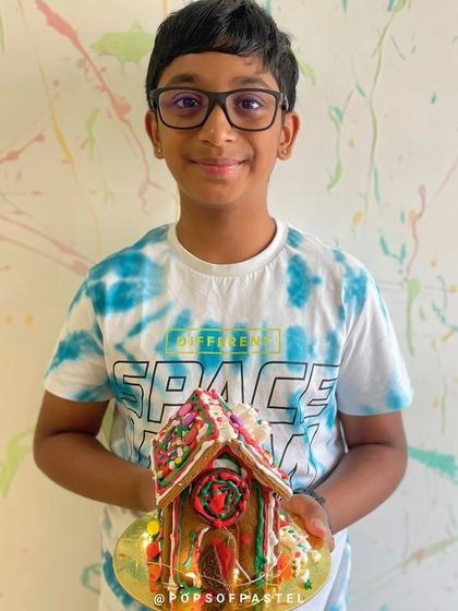 A young boy proudly holds up the incredibly detailed gingerbread house he decorated, a true holiday masterpiece.